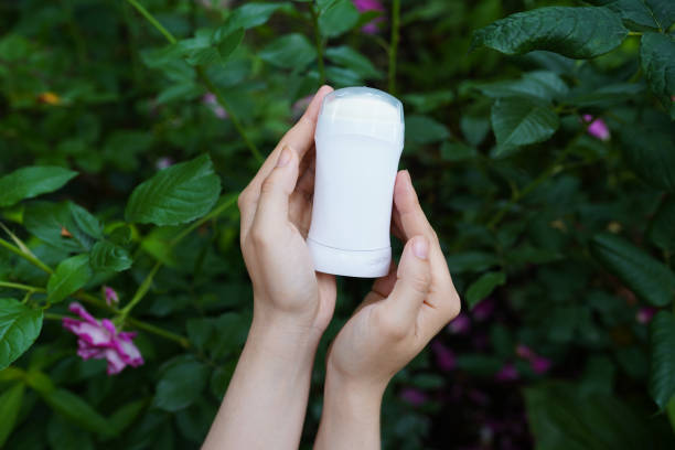 Hands holding a white deodorant stick against a backdrop of green leaves and pink flowers