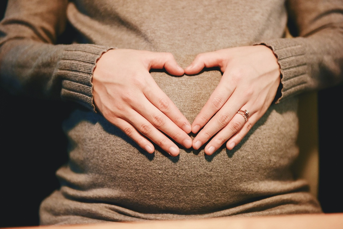A pregnant woman making a heart with her hands on her belly.