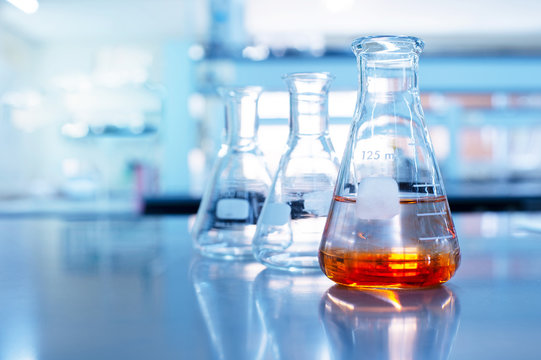 Laboratory glassware with clear and orange liquid on a reflective surface